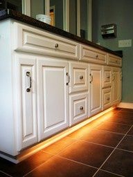 a bathroom with white cabinets and lights on the counter top in front of it is tiled flooring