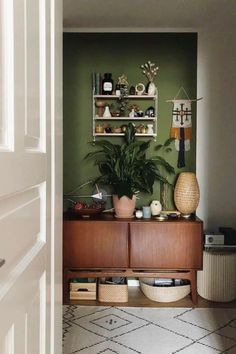 a green wall with shelves and plants on it in a room next to a door