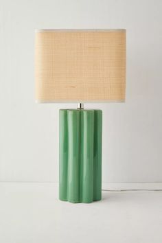 a green table lamp sitting on top of a white floor next to a beige shade