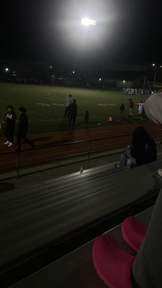 people are sitting on the bleachers watching a game at night with bright lights