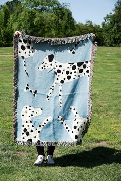 a person standing in the grass holding a blanket with dalmatian dogs on it