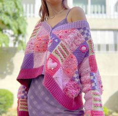 a woman wearing a purple sweater with pink and green designs on it, standing in front of a building