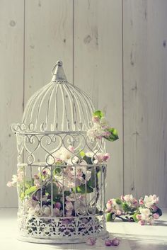 a white birdcage filled with flowers on top of a table