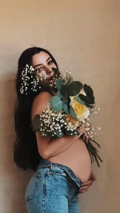 a pregnant woman with flowers in her hair and jeans on the belly, standing next to a wall