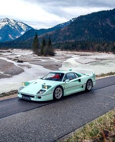 a green sports car driving down a road next to a river and mountains in the background