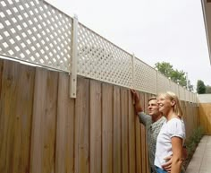 a man and woman standing next to each other near a wooden fence with lattice design on it