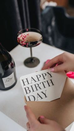 a woman holding a piece of paper with the words happy birth day on it next to a bottle of wine