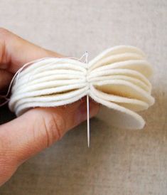 a hand holding a piece of white yarn with a needle in it's center