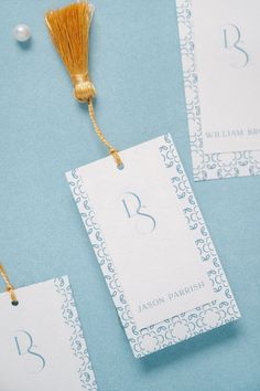 three place cards with tassels on top of each one and two pearls in the background