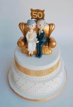 a 50th cake with an old couple sitting on a chair and the number 50 is gold