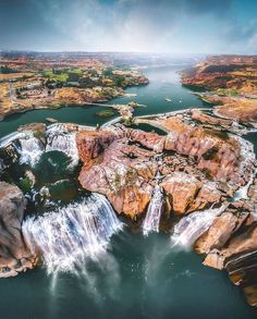 an aerial view of a waterfall in the middle of a lake surrounded by rocks and water