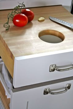 two tomatoes and a knife on a cutting board next to an open drawer with drawers