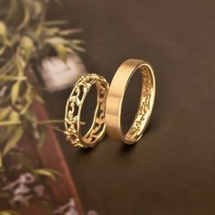 two gold wedding rings sitting next to each other on top of a wooden table with flowers in the background