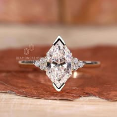 an engagement ring with a pear shaped diamond in the center on top of a piece of wood