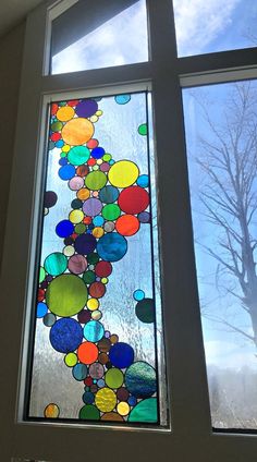 two windows with different colored glass balls on the window sill and one has a tree in the background