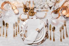 the table is set with gold and white plates, silverware, and napkins