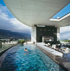 a person swimming in a large pool next to a tall building with a bar on top