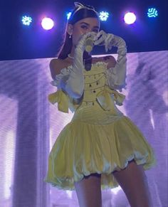 a woman in a yellow dress on stage with her hands up to her face and one hand over her mouth