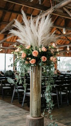 a tall vase filled with flowers and greenery on top of a wooden table covered in chairs