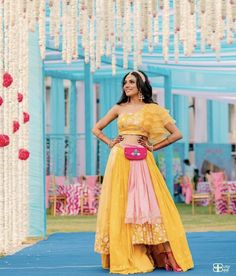 a woman in a yellow and pink dress standing on a blue stage with flowers hanging from the ceiling