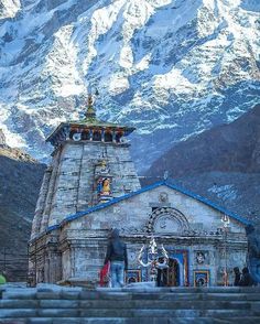 people are standing in front of a building with snow covered mountains behind it