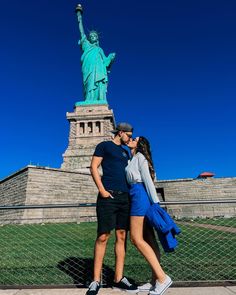 a man and woman standing in front of the statue of liberty