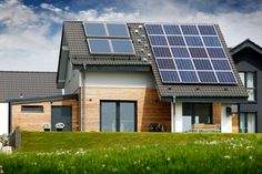 a house with solar panels on the roof and grass in front of it, against a blue sky