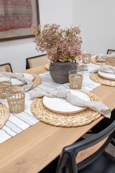 a dining table set with place settings and flowers in a vase on the table top