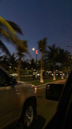 a car driving down the street at night with palm trees in the backgroud