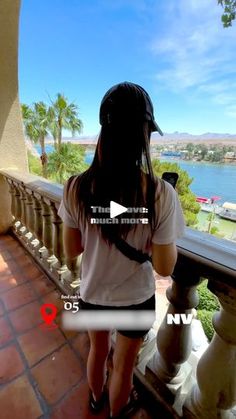 a woman is standing on a balcony looking out at the water and palm trees in front of her