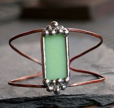 a close up of a bracelet with a green glass bead on the front and back