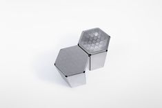 two silver boxes sitting side by side on a white surface, one is shaped like an octagon