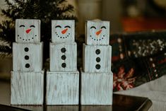 three snowmen made out of wooden blocks sitting on a table next to a christmas tree