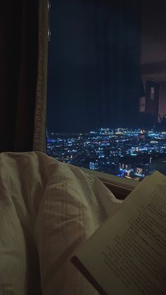 an open book sitting on top of a bed in front of a window at night