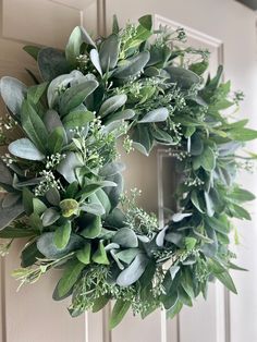 a wreath hanging on the front door of a house with greenery and leaves around it