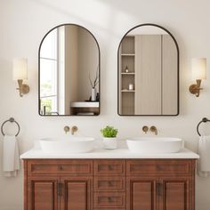 two oval mirrors are above the double sinks in this bathroom with white walls and wood cabinetry