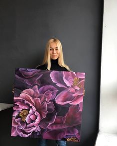 a woman holding up a large painting with purple flowers on it