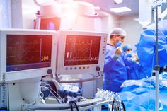 medical equipment in an operating room with doctors working on the monitor and monitors showing heartbeats