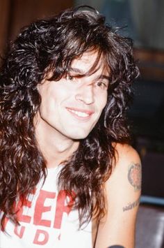 a man with long curly hair wearing a t - shirt and looking at the camera