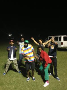 four young men standing in the grass with their arms up and one holding his hand out