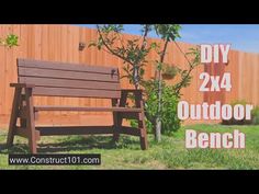 a wooden bench sitting in the grass next to a tree and fence with an advertisement on it