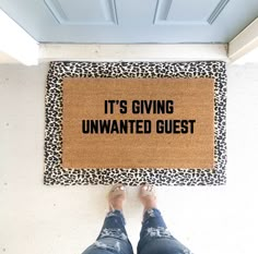 a person standing in front of a door mat that says it's giving unwanted guest