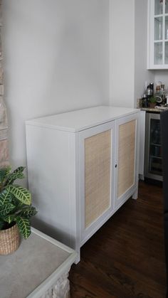 a white cabinet in a kitchen next to a potted plant