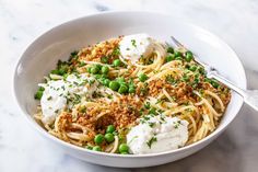 a bowl filled with pasta and peas on top of a marble countertop next to a fork