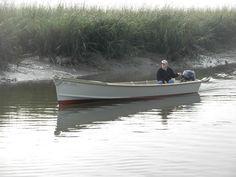 two people in a small boat on the water near some grass and sand shore line