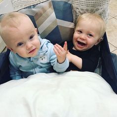 two baby boys sitting in a suitcase on the floor and one is smiling at the camera