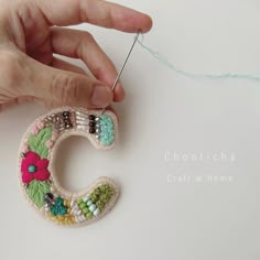 someone is making a beaded brooch that looks like the letter c with flowers on it