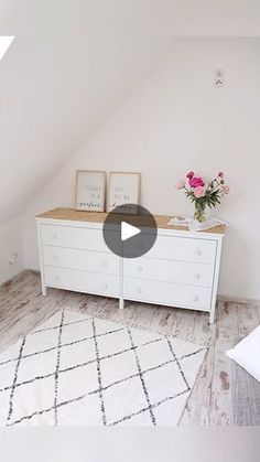 a white dresser sitting in the corner of a room next to a vase with flowers