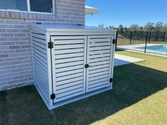 a white storage shed sitting in the grass next to a brick wall and swimming pool