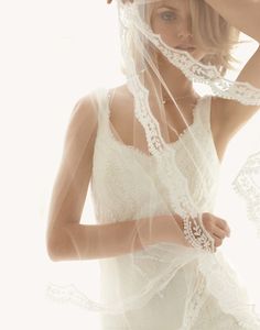 a woman in a white dress with a veil over her head and hands behind her head